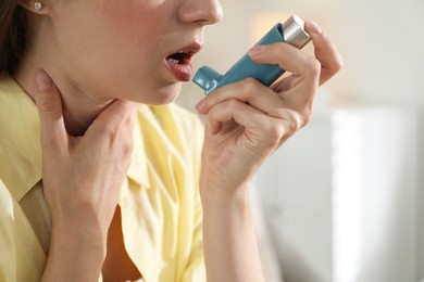 Young woman using asthma inhaler at home, closeup