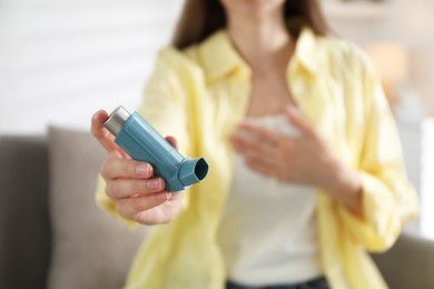 Woman holding asthma inhaler indoors, selective focus