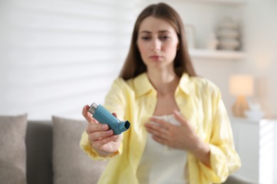 Woman holding asthma inhaler indoors, selective focus