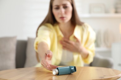 Photo of Young woman with asthma inhaler at table, selective focus