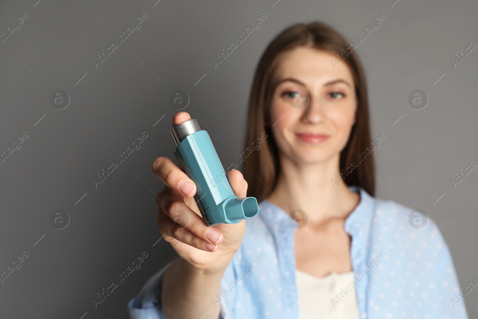 Photo of Young woman using asthma inhaler on grey background, selective focus