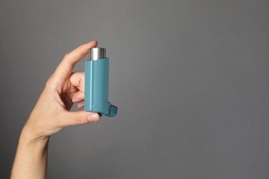 Photo of Woman holding asthma inhaler on grey background, closeup. Space for text