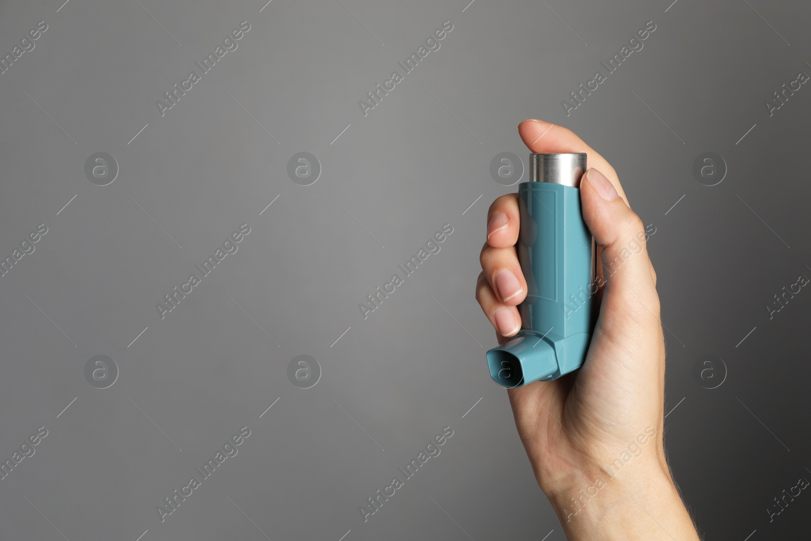 Photo of Woman holding asthma inhaler on grey background, closeup. Space for text