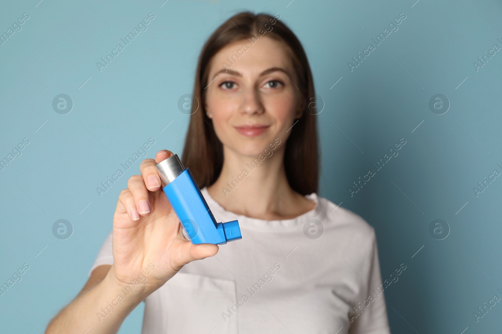 Photo of Young woman holding asthma inhaler on light blue background, selective focus