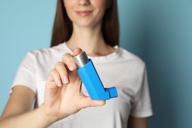 Photo of Woman holding asthma inhaler on light blue background, selective focus