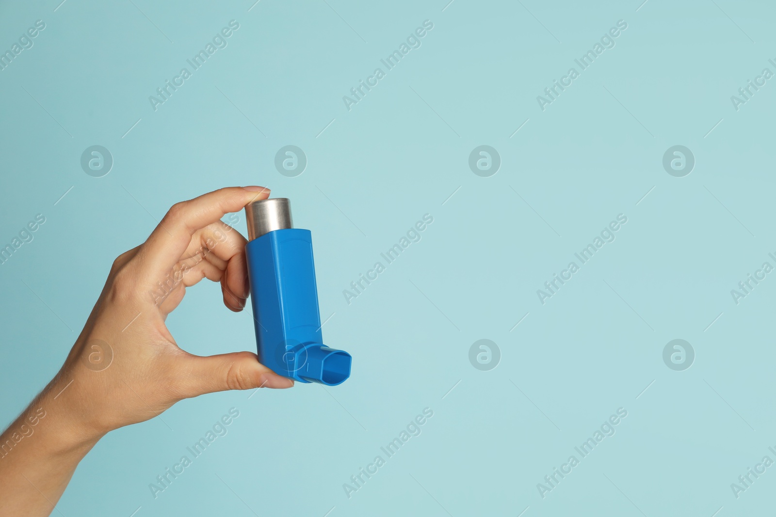 Photo of Woman holding asthma inhaler on light blue background, closeup. Space for text