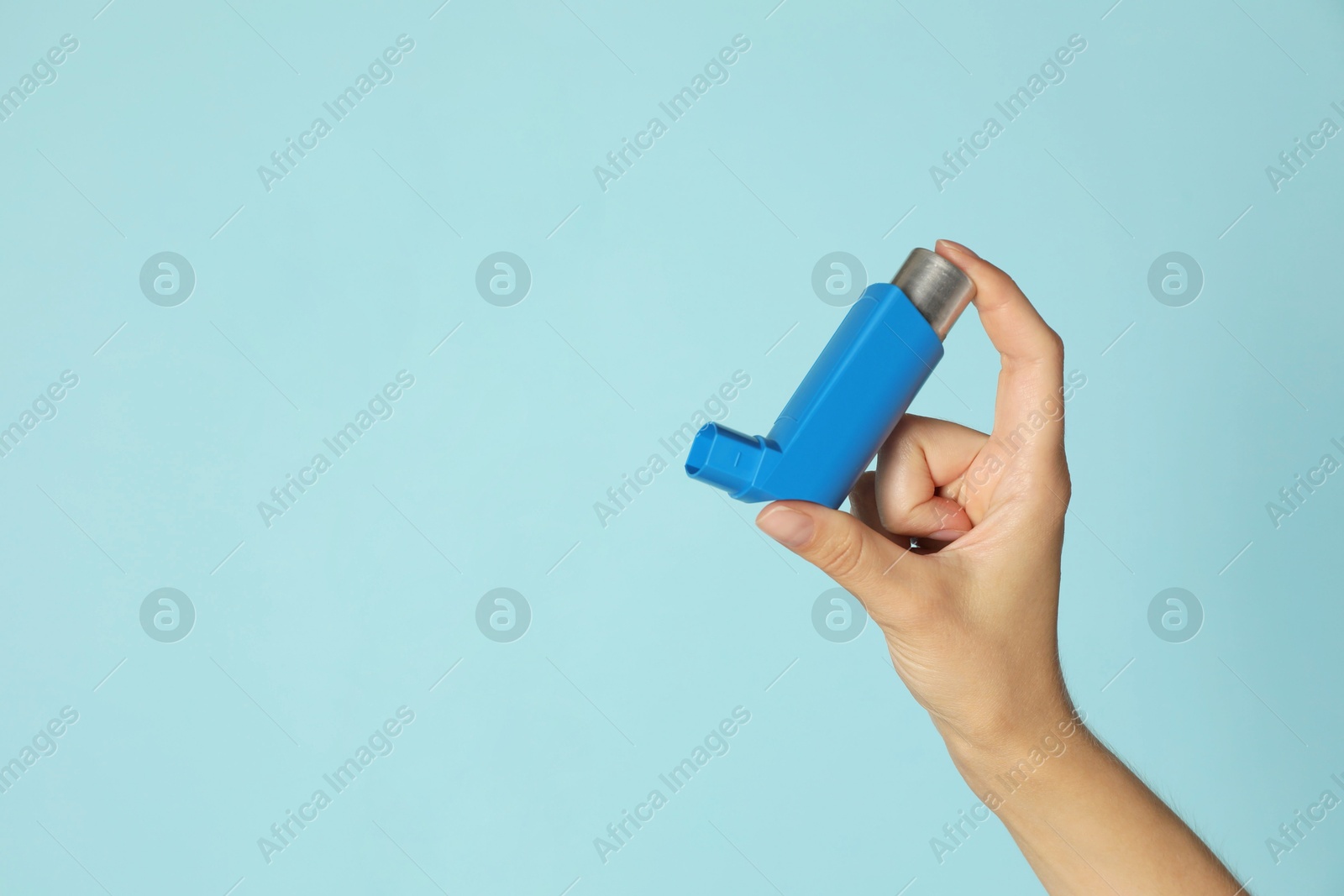 Photo of Woman holding asthma inhaler on light blue background, closeup. Space for text