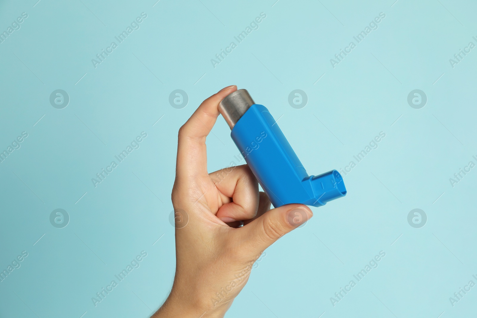 Photo of Woman holding asthma inhaler on light blue background, closeup