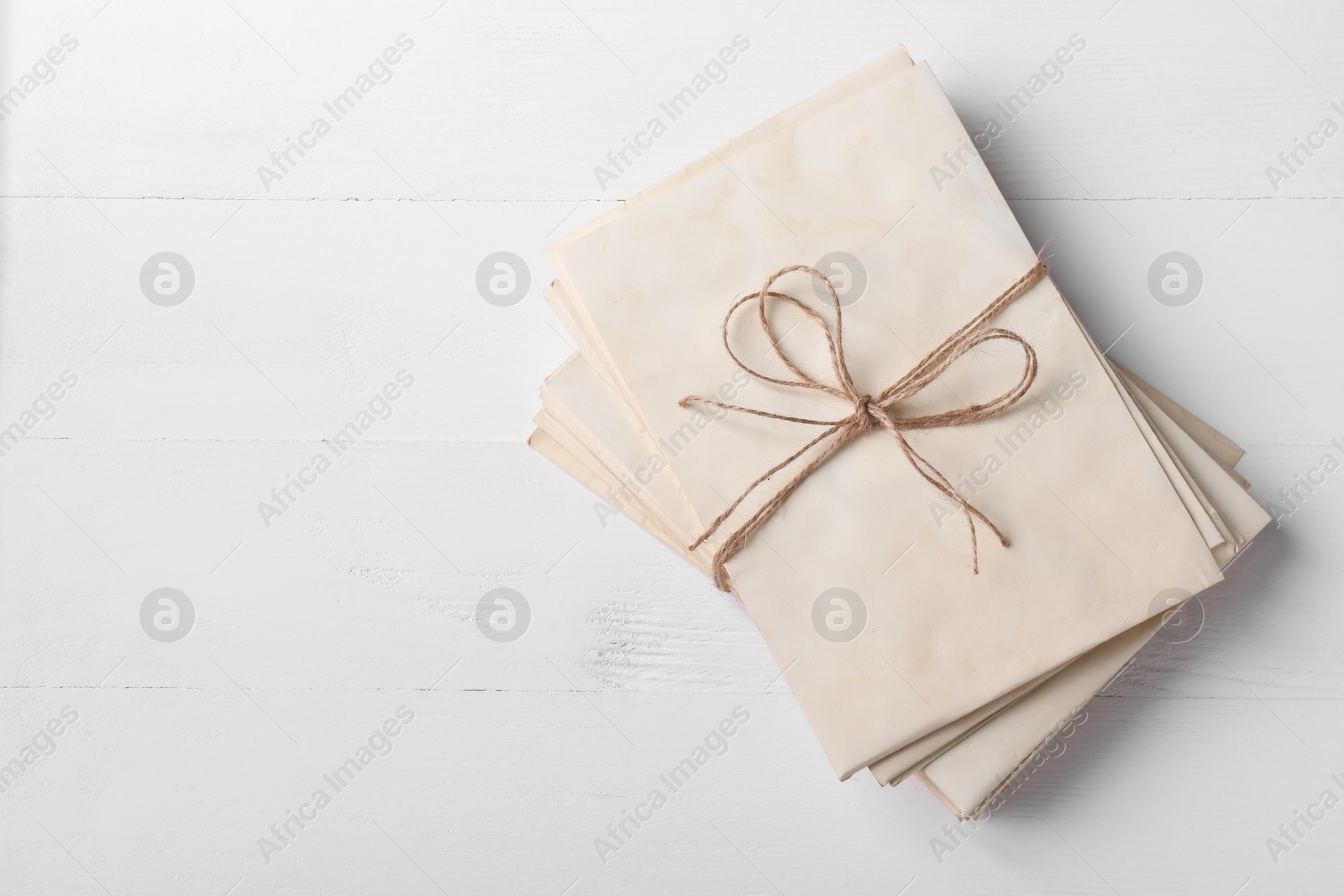 Photo of Stack of old letters tied with twine on white wooden table, top view. Space for text