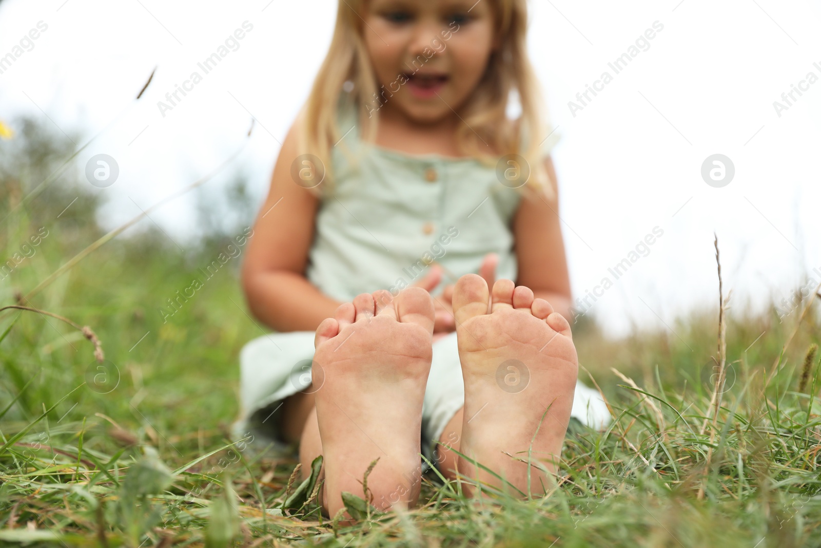 Photo of Barefoot little girl on green grass at meadow, selective focus. Child enjoying beautiful nature