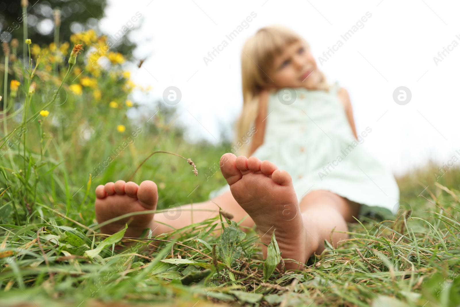 Photo of Barefoot little girl on green grass at meadow, selective focus. Child enjoying beautiful nature