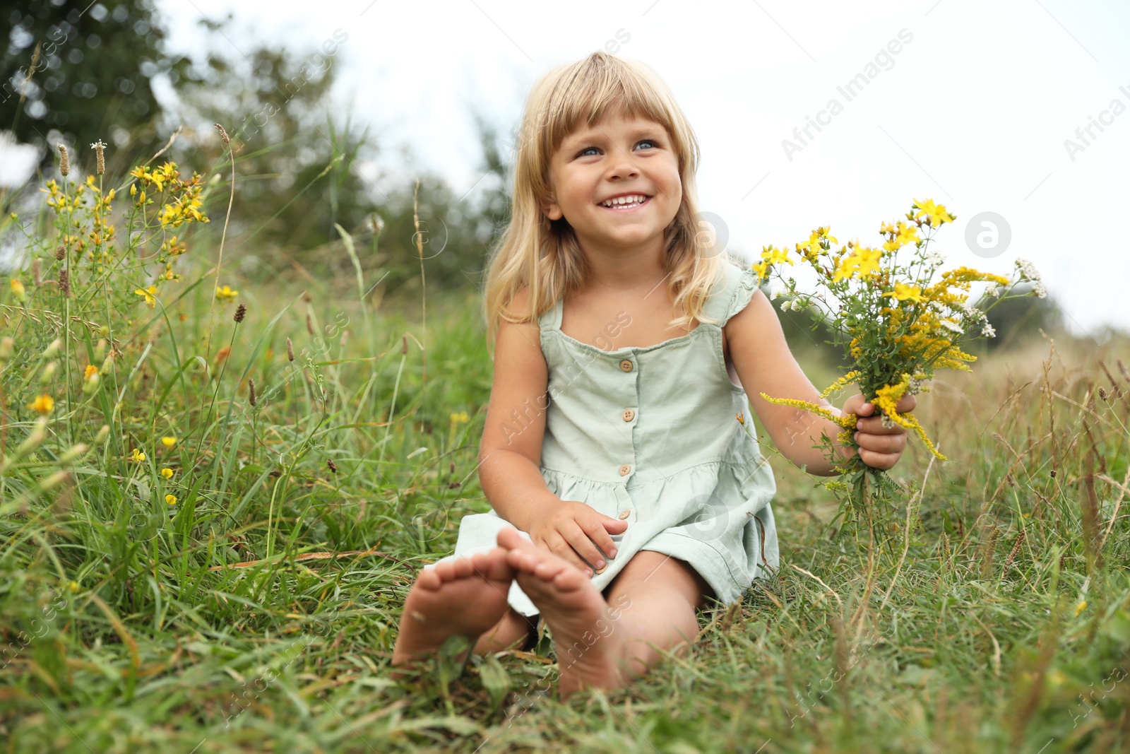 Photo of Barefoot little girl with flowers at meadow. Child enjoying beautiful nature