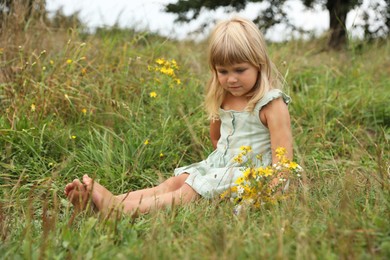 Barefoot little girl with meadow flowers on green grass. Child enjoying beautiful nature