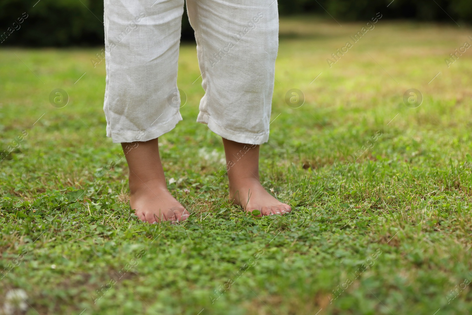 Photo of Little child standing barefoot on green grass outdoors, closeup. Enjoying nature