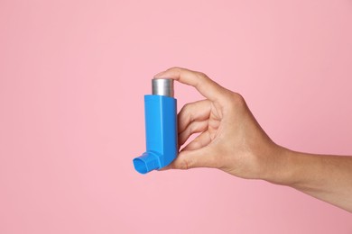 Photo of Woman holding asthma inhaler on pink background, closeup