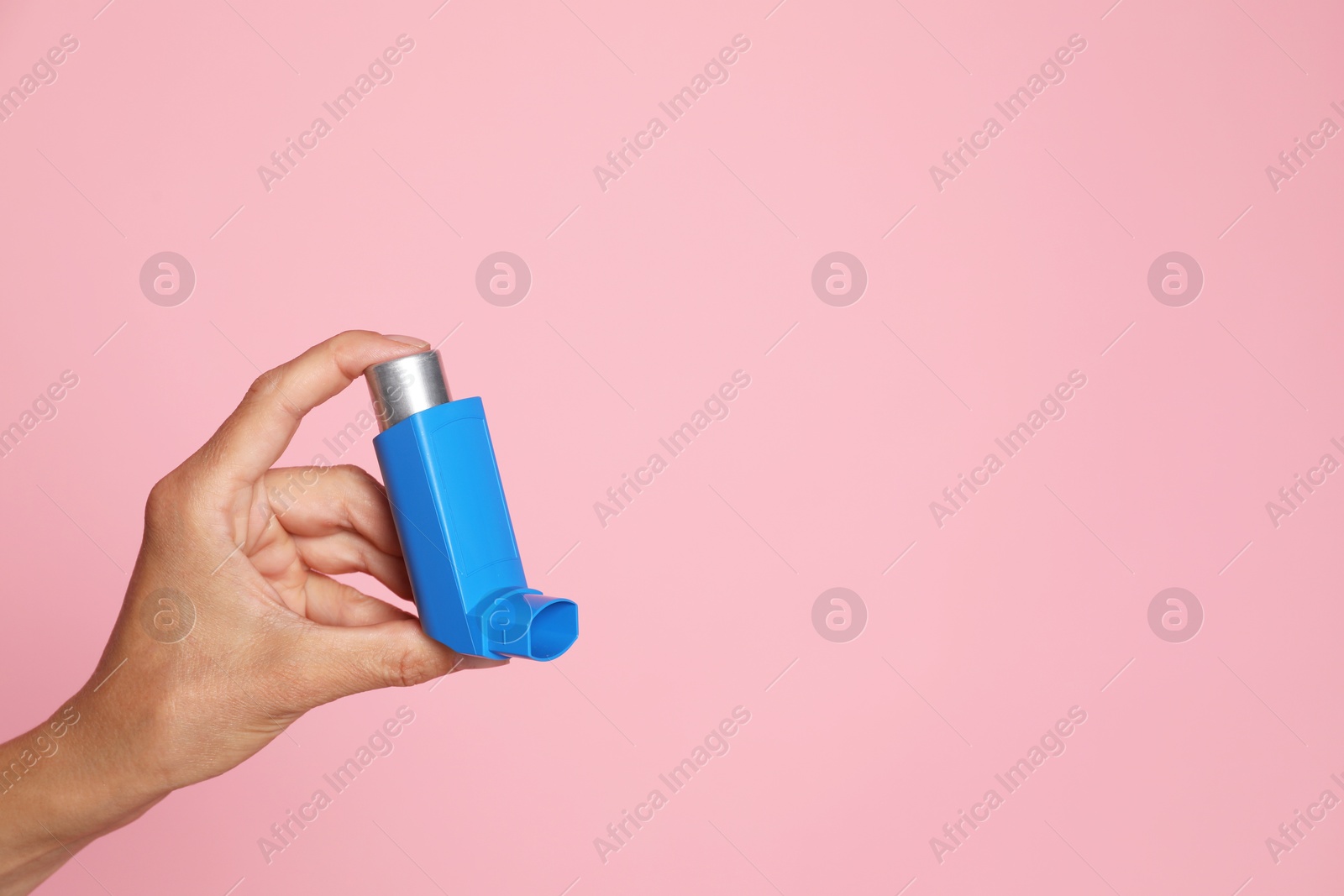 Photo of Woman holding asthma inhaler on pink background, closeup. Space for text