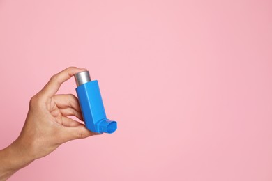 Photo of Woman holding asthma inhaler on pink background, closeup. Space for text