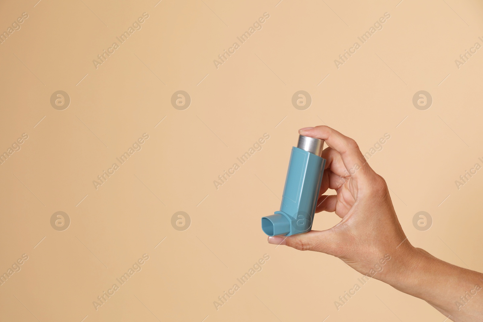 Photo of Woman holding asthma inhaler on beige background, closeup. Space for text