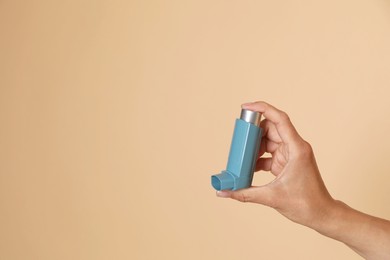 Woman holding asthma inhaler on beige background, closeup. Space for text