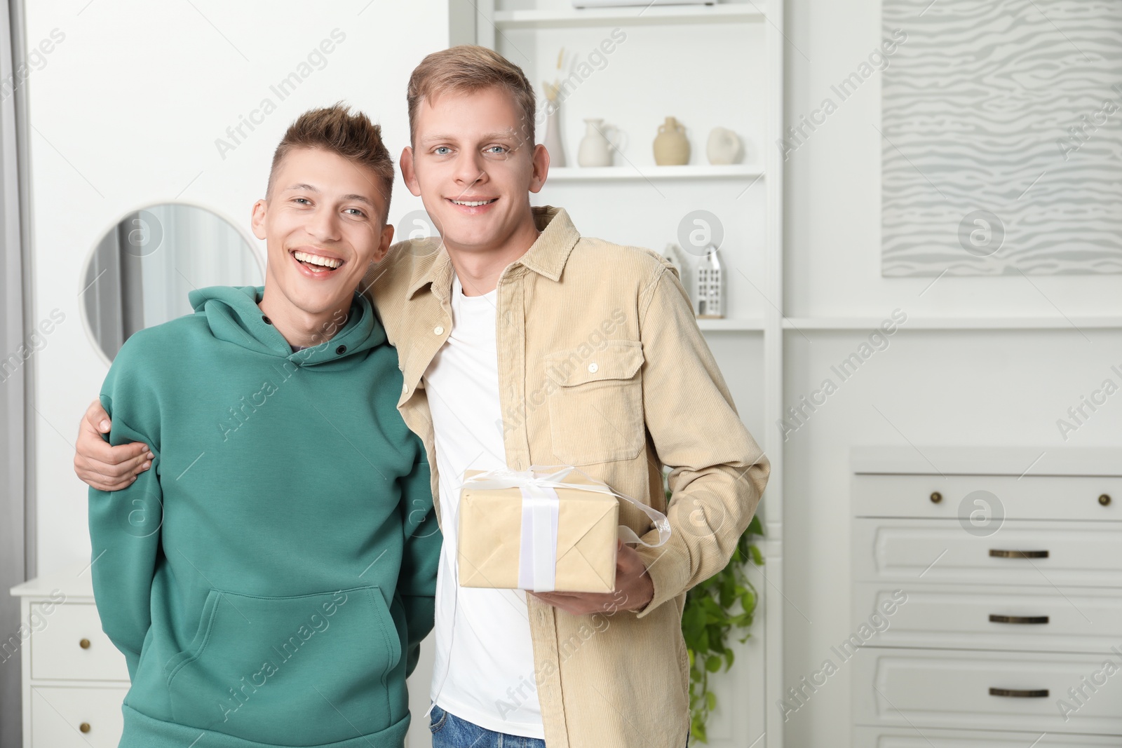 Photo of Family portrait of happy brothers with gift box at home. Space for text