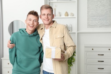 Family portrait of happy brothers with gift box at home. Space for text