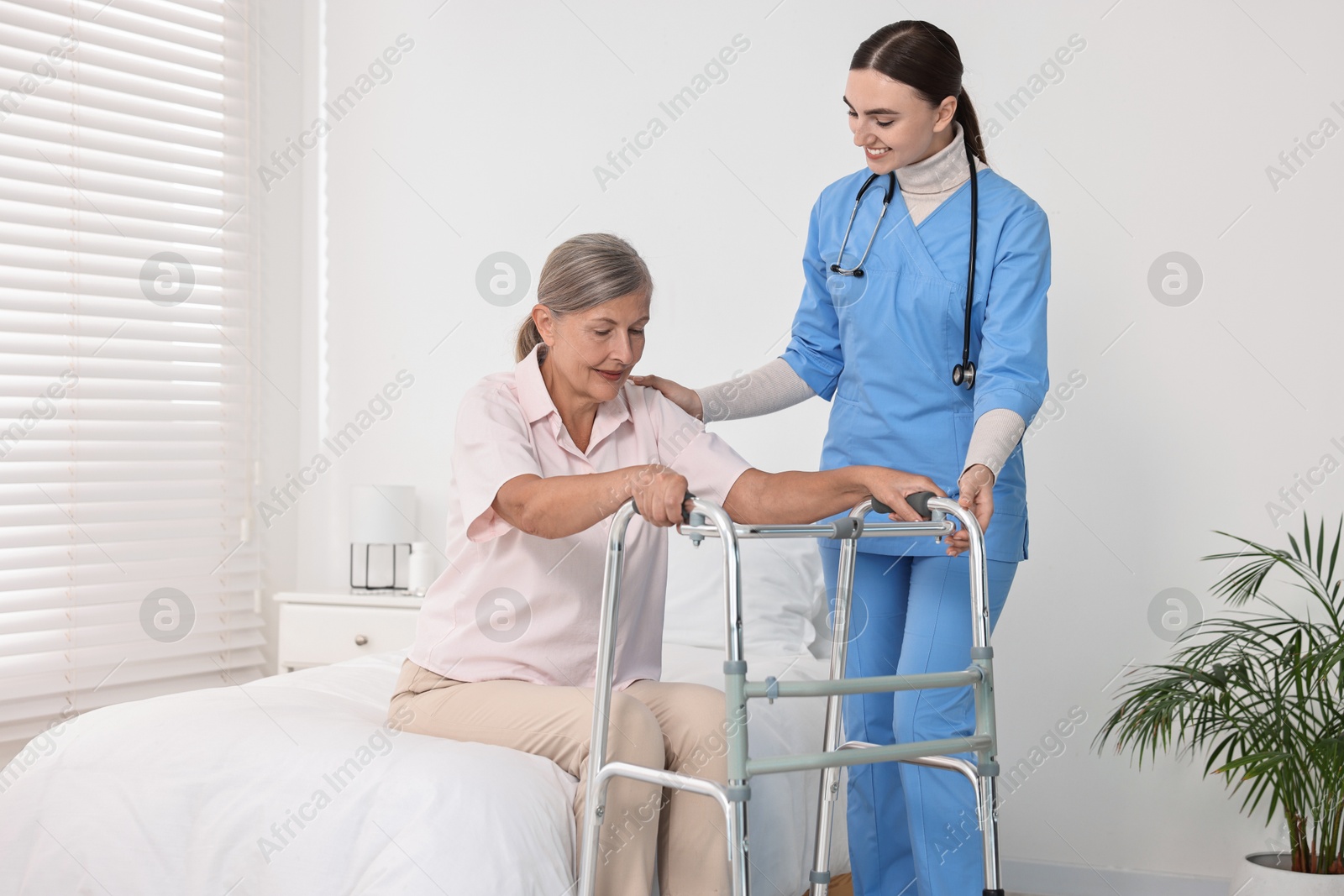 Photo of Nurse helping senior woman with walking frame in clinic