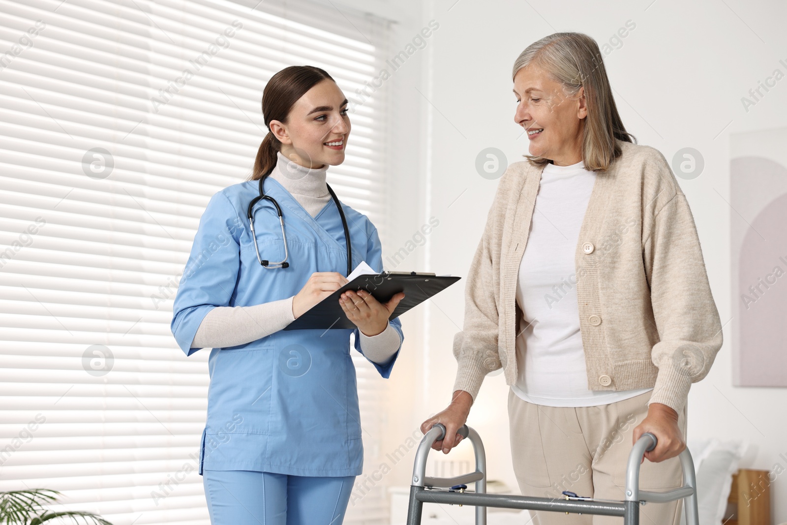 Photo of Nurse helping senior woman with walking frame in clinic