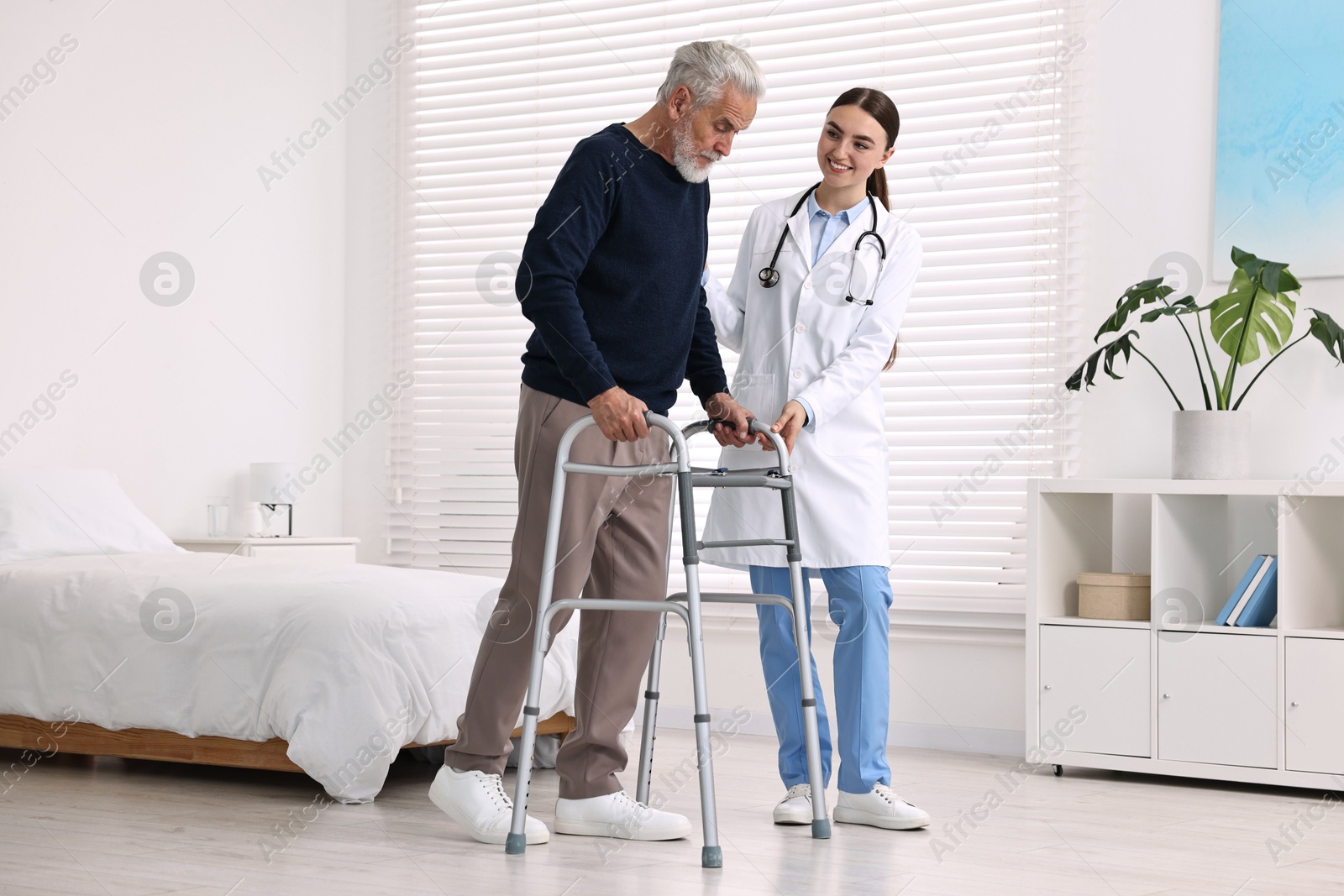 Photo of Doctor helping senior man with walking frame in clinic