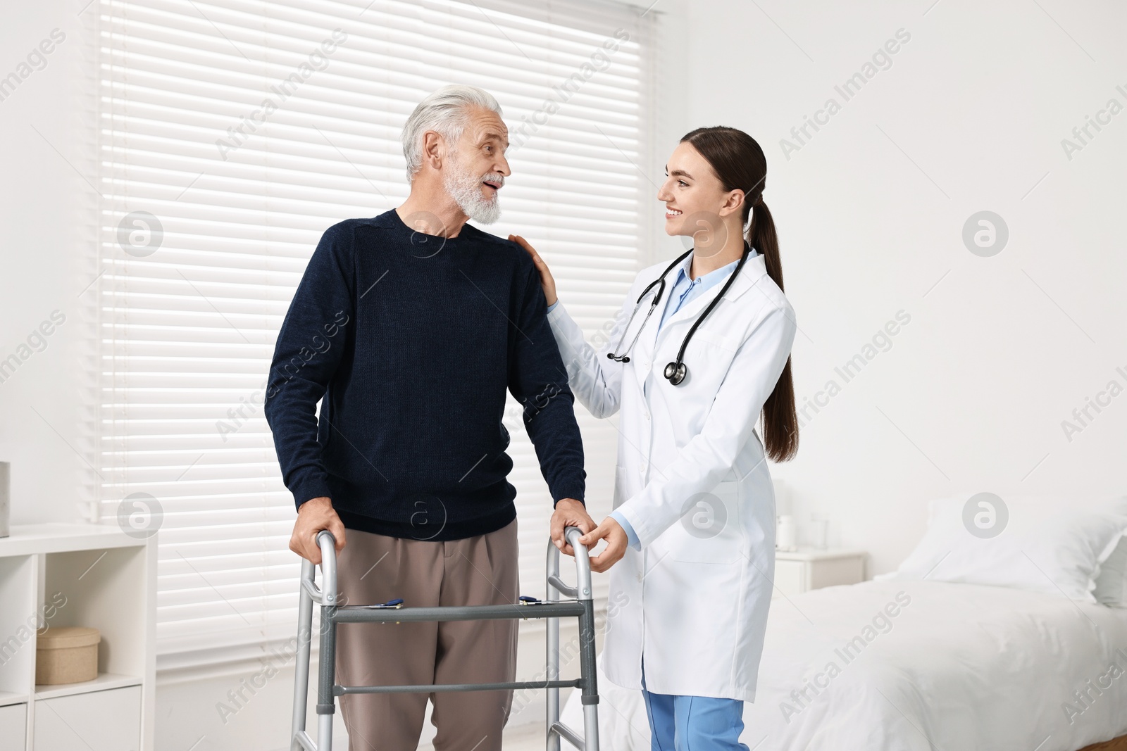 Photo of Doctor helping senior man with walking frame in clinic