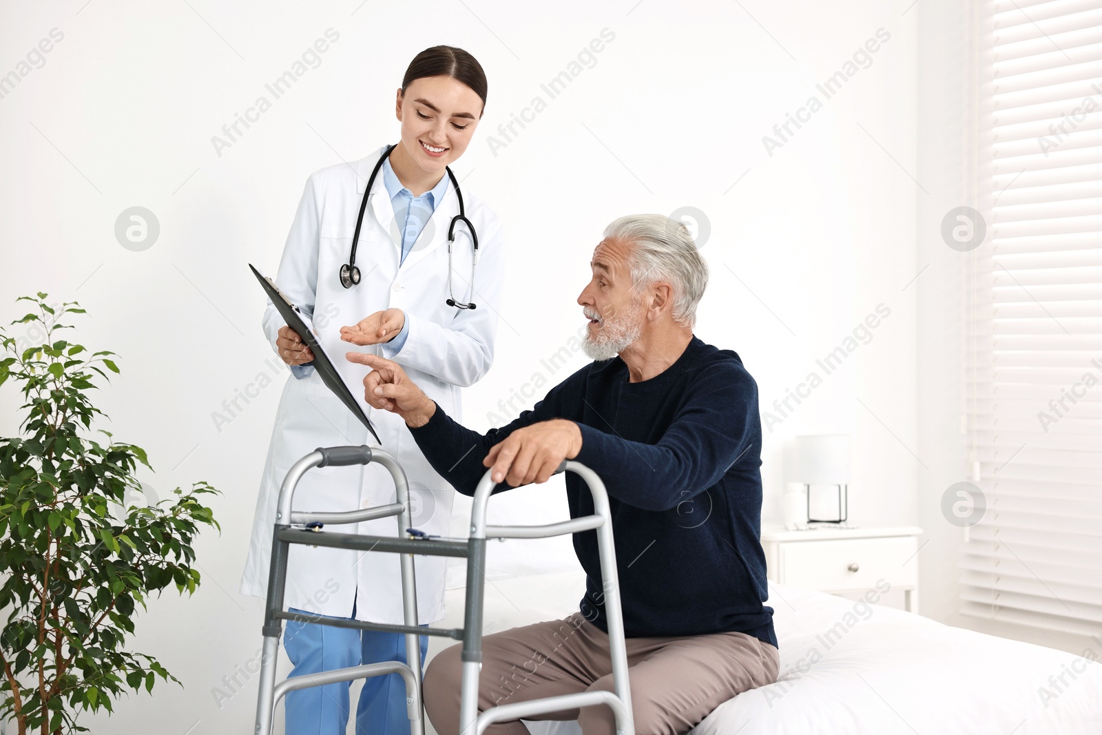 Photo of Doctor consulting senior patient with walking frame in hospital ward