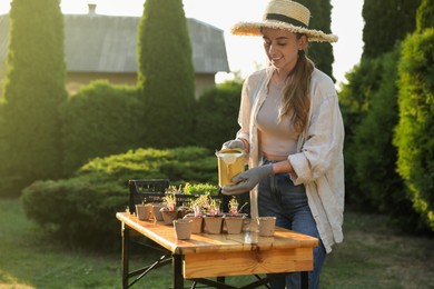 Smiling woman watering potted seedlings with can at table outdoors