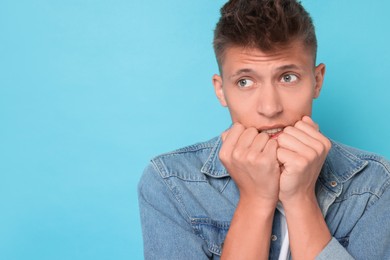 Portrait of scared young man on light blue background, space for text