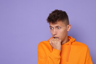 Portrait of scared young man on violet background, space for text