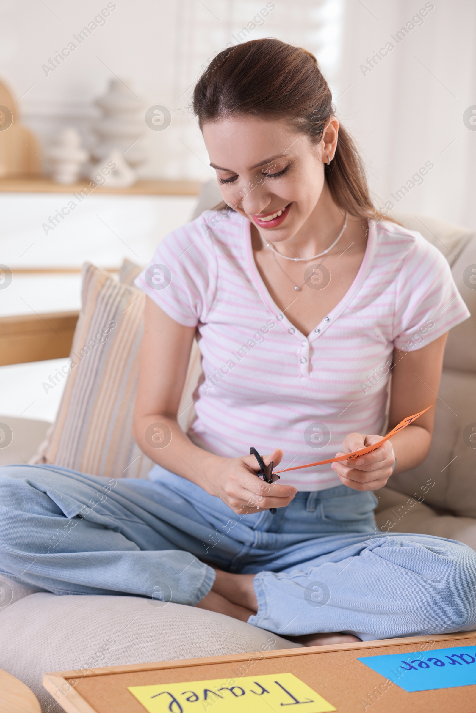 Photo of Creating vision board. Woman cutting card on sofa indoors