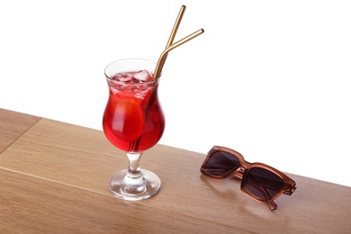 Photo of Glass of tasty refreshing drink, straws and sunglasses on wooden table against white background