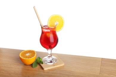 Glass of tasty refreshing drink with straw and fresh fruit on wooden table against white background