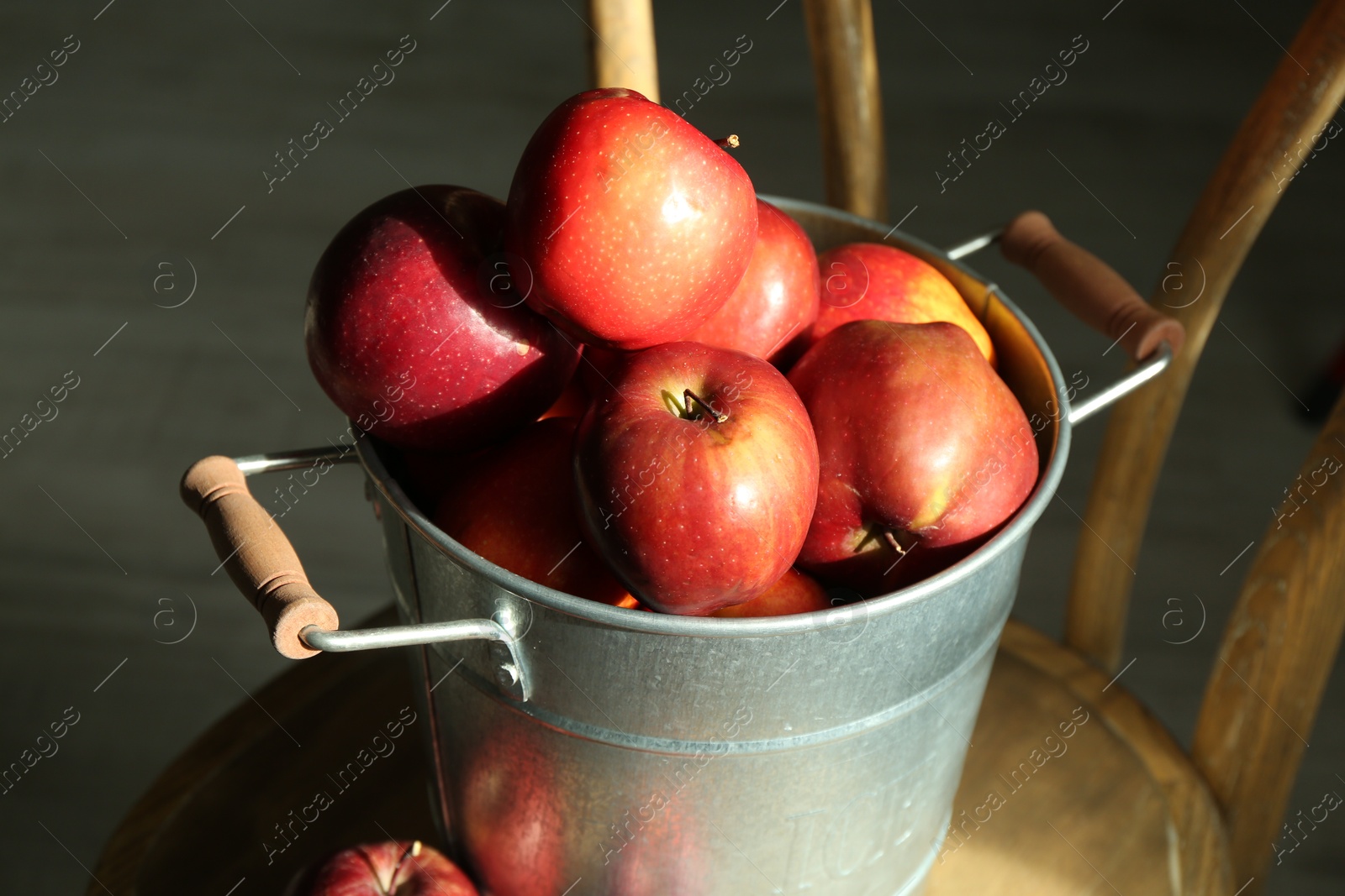 Photo of Fresh ripe red apples in bucket on wooden chair