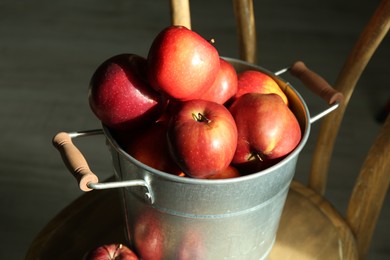 Photo of Fresh ripe red apples in bucket on wooden chair