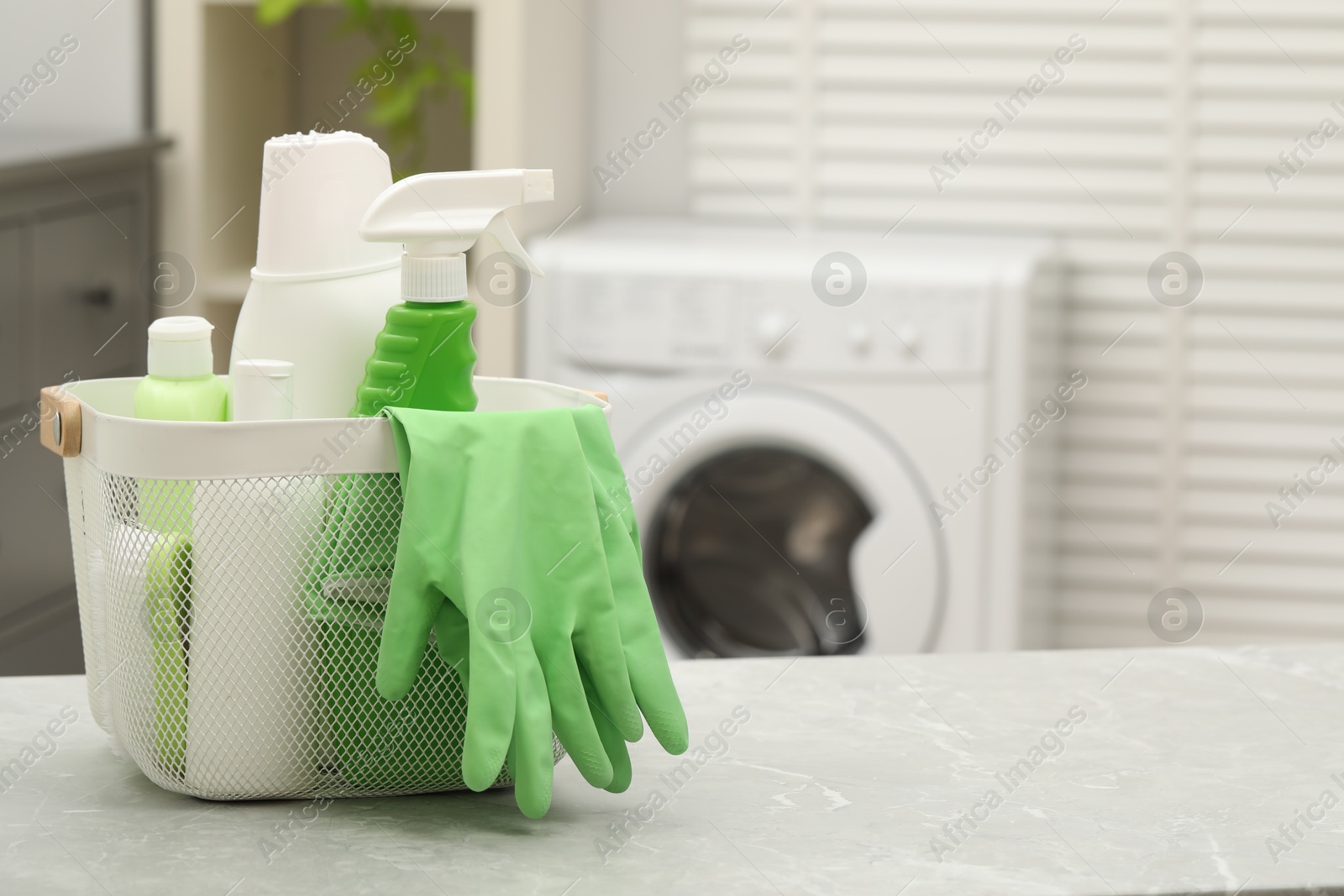 Photo of Different laundry detergents, rubber gloves and sponge in basket on light grey marble table indoors. Space for text