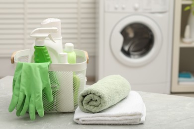 Photo of Different laundry detergents, rubber gloves and terry towels on light grey marble table in bathroom