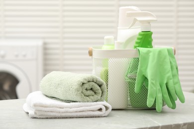 Photo of Different laundry detergents, rubber gloves and terry towels on light grey marble table in bathroom