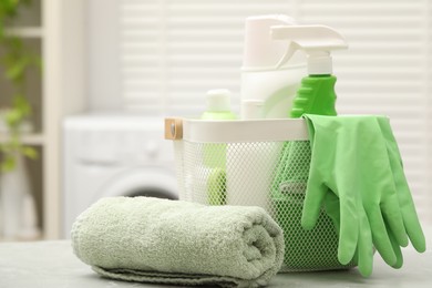 Photo of Different laundry detergents, rubber gloves and rolled towel on light table in bathroom