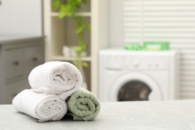 Photo of Rolled terry towels on wooden table in laundry room. Space for text