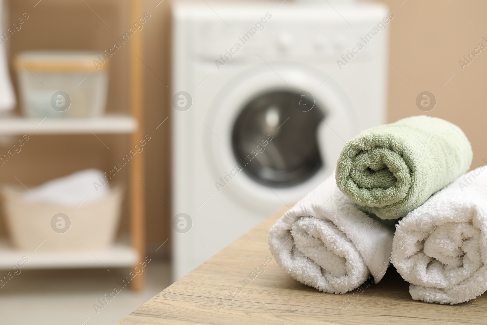 Photo of Rolled terry towels on wooden table in laundry room. Space for text