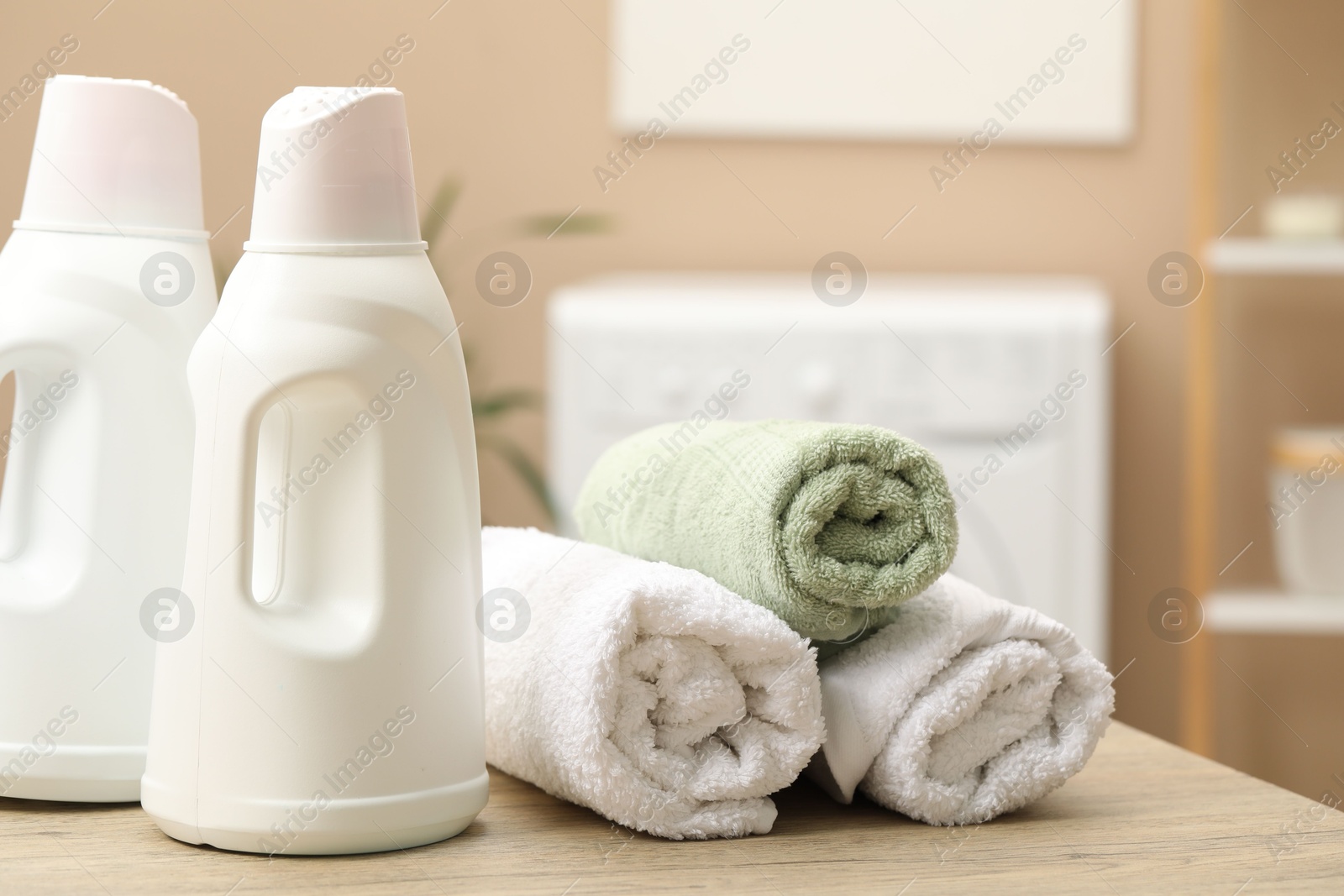 Photo of Laundry detergents and rolled towels on wooden table in bathroom