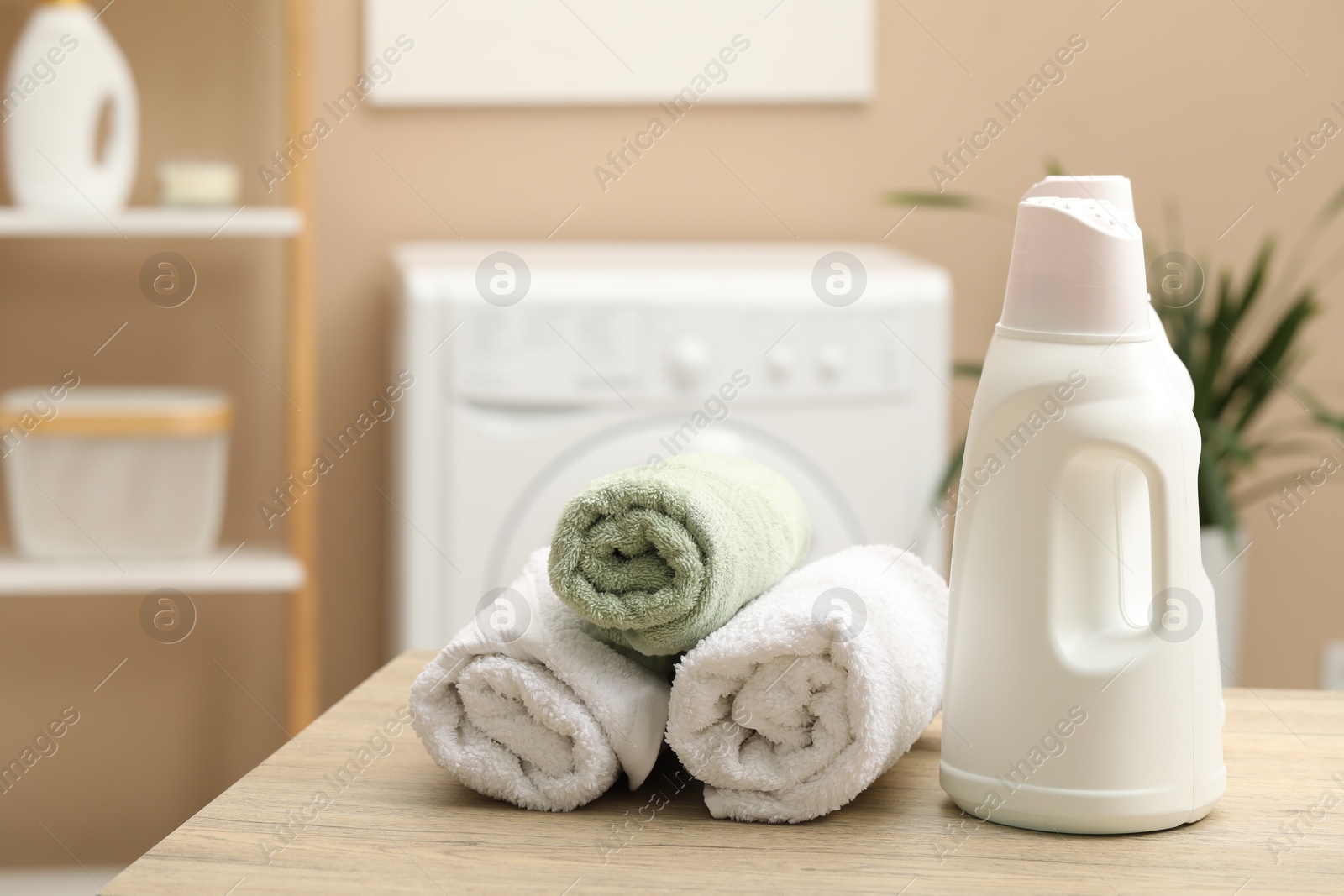 Photo of Laundry detergent and rolled towels on wooden table in bathroom. Space for text