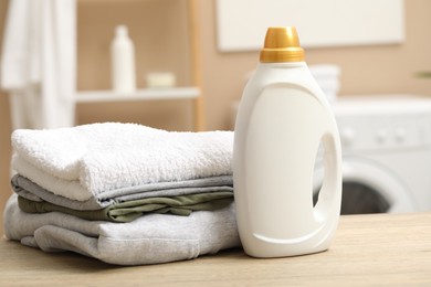 Photo of Laundry detergent and stacked terry towels on wooden table in bathroom