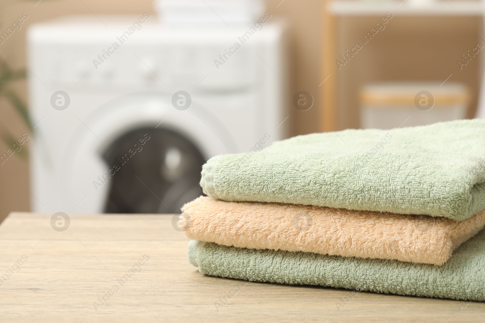 Photo of Stack of terry towels on wooden table in laundry room, closeup. Space for text