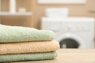 Photo of Stack of terry towels on wooden table in laundry room, closeup. Space for text