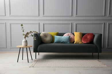 Photo of Stylish sofa with cushions and eucalyptus branches in vase on side table near grey wall